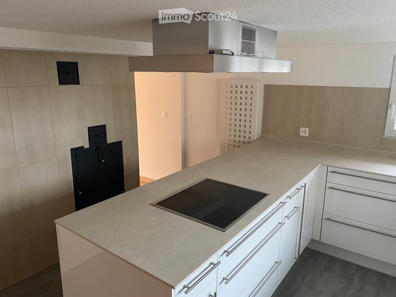 Modern kitchen with white cabinets, a central island, and an induction stove. Features a stainless steel range hood and sleek design.