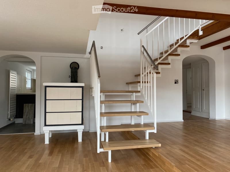 Spacious hallway with wooden flooring, white walls, and a staircase leading to an upper level. Features include a built-in storage unit and an arched doorway leading to another room.