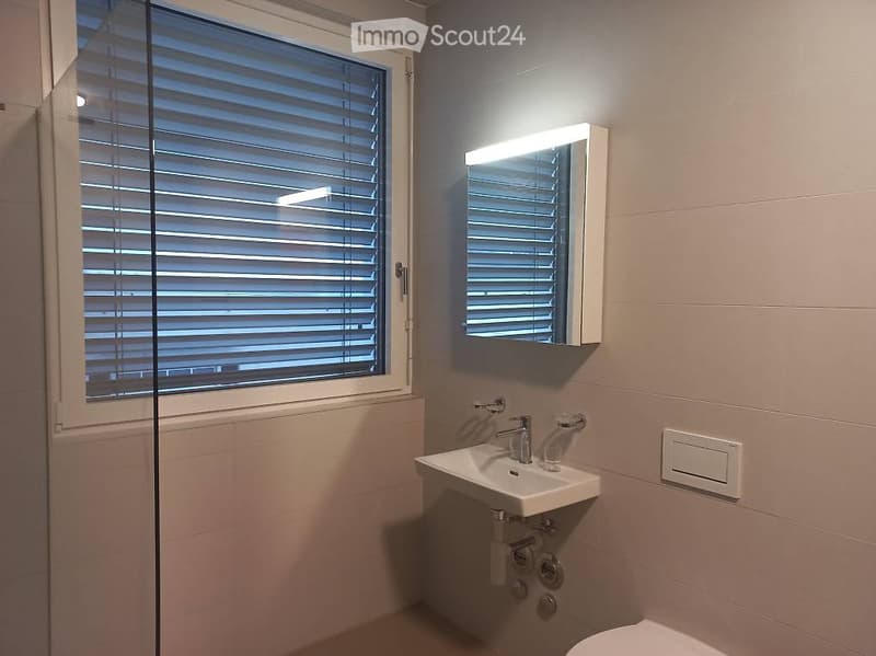 Modern bathroom with a white sink, chrome faucet, illuminated mirror, and window with blinds.