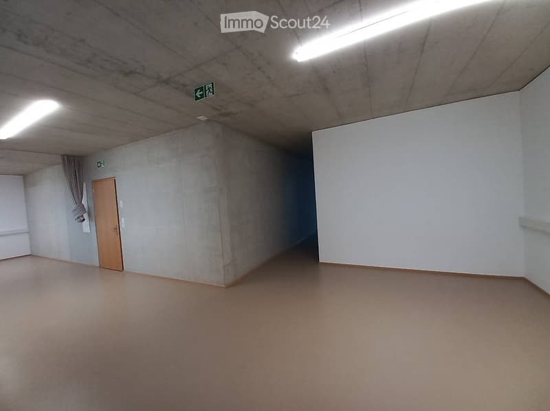 Empty room with concrete walls, wooden door, and fluorescent lighting. No furniture or equipment present.