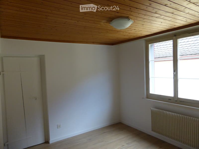 Empty room with wooden flooring, white walls, a single window with white frame, a radiator, and a built-in wardrobe.