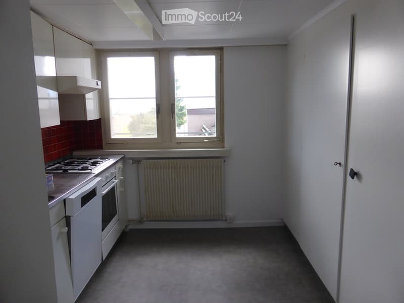 Empty kitchen with white cabinets, a gas stove, and a window overlooking an outdoor area.