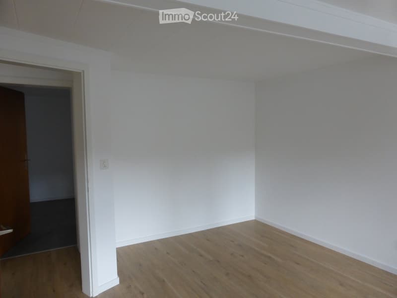 Empty room with white walls and wooden flooring, featuring a doorway leading to another space.