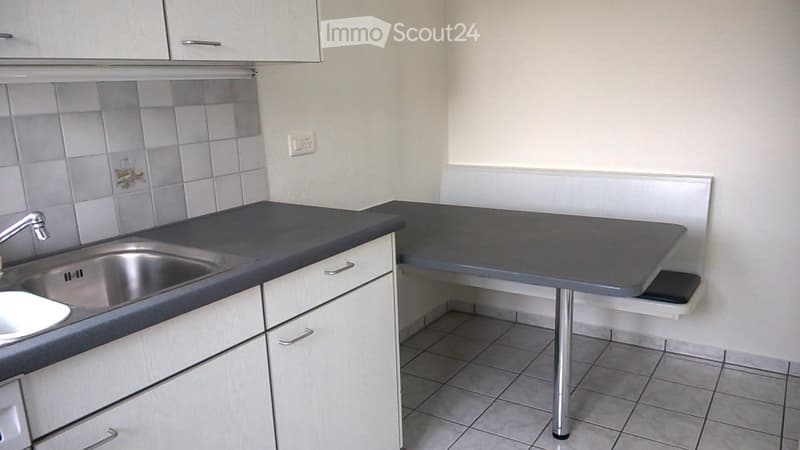 Modern kitchen with white cabinets, grey countertop, stainless steel sink, and a small table with a stool.