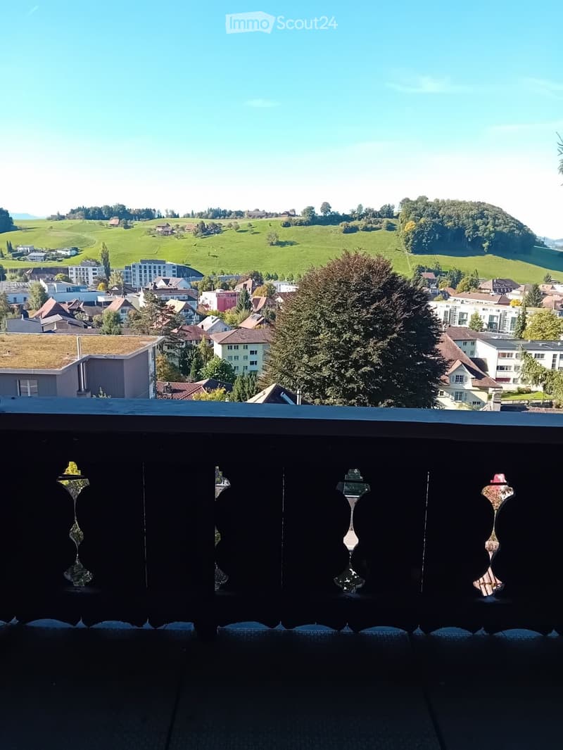Balcony overlooking a scenic town with houses, green hills, and a clear blue sky.
