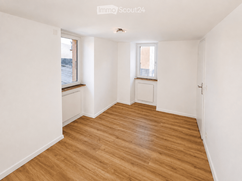 Empty room with light wooden flooring, white walls, and two windows. No furniture or equipment present.