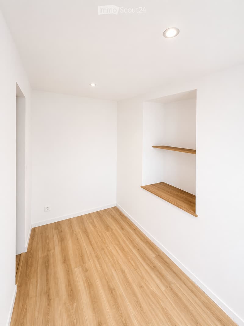 Empty room with white walls, wooden flooring, and a small built-in wooden shelf unit.