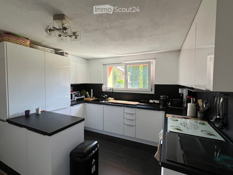 Modern kitchen with white cabinets, black countertops, and stainless steel appliances. Features include a refrigerator, sink, coffee maker, toaster, and various kitchen utensils.