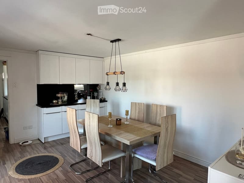 Modern kitchen with white cabinets, a wooden dining table, six chairs, and decorative candles on the table.