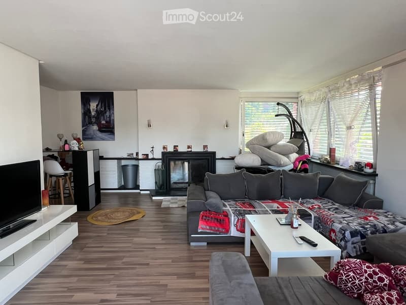 Modern living room with a grey sectional sofa, coffee table, TV, fireplace, and a small dining area with stools.