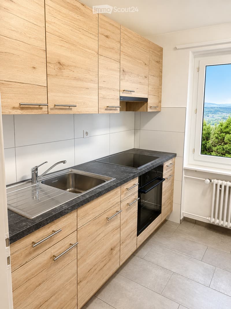 Modern kitchen with light wooden cabinets, black countertop, stainless steel sink, and built-in oven. Large window offers a scenic view.