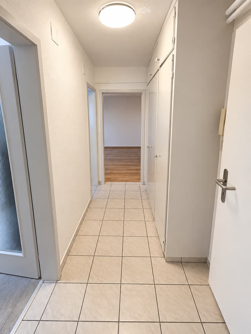 Clean, well-lit hallway with tiled flooring and white walls, featuring several doors and a recessed ceiling light.