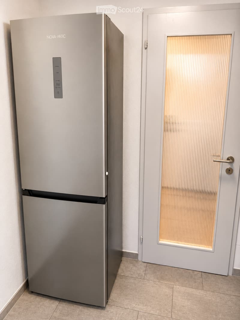 Modern stainless steel refrigerator with digital display, positioned next to a frosted glass door with vertical blinds.