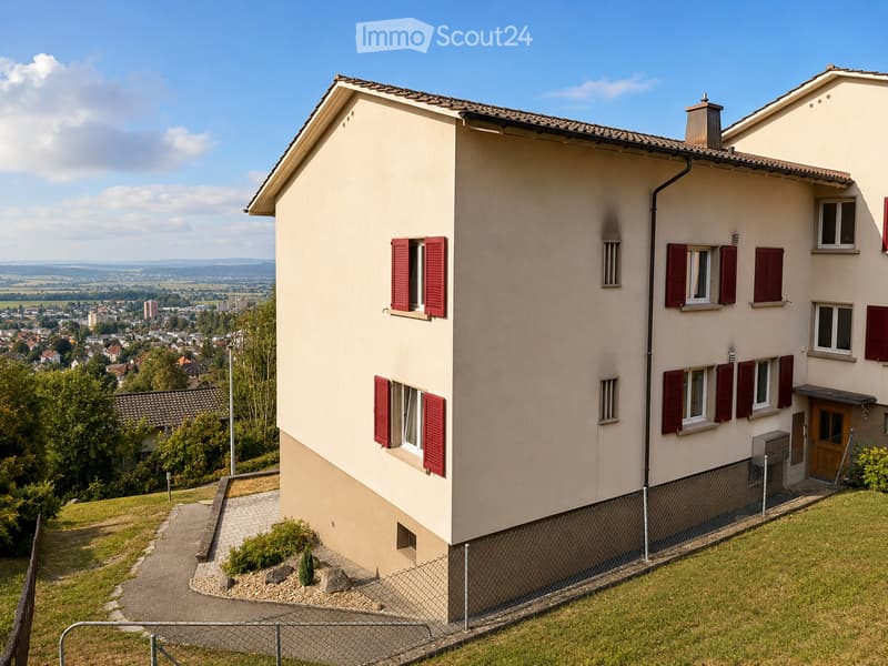 Two-story house with beige walls, red shutters, and a tiled roof, situated on a hillside with a view of a town and landscape.
