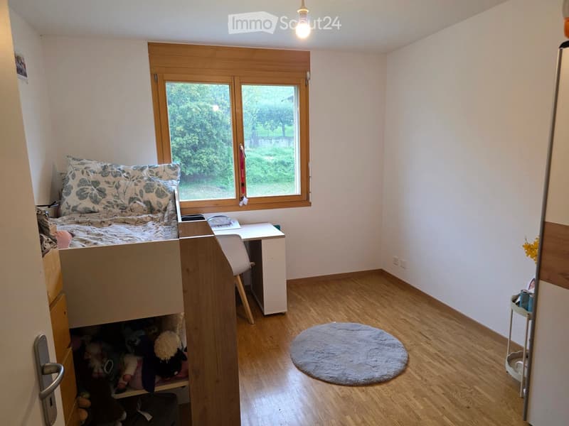 Cozy bedroom with a lofted twin-sized bed, a small desk with a chair, a round rug, and a storage unit filled with stuffed animals.