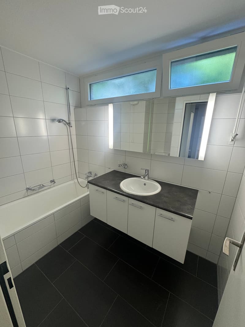 Modern bathroom with white tiled walls, black tiled floor, bathtub, sink, mirror, and built-in cabinets.