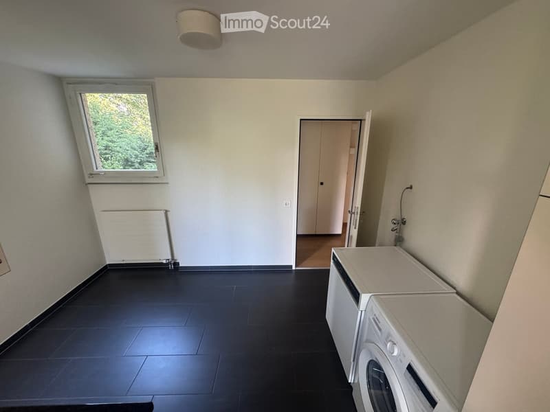 Empty room with black tiled floor, white walls, a window, and a washing machine and dishwasher placed against the wall.
