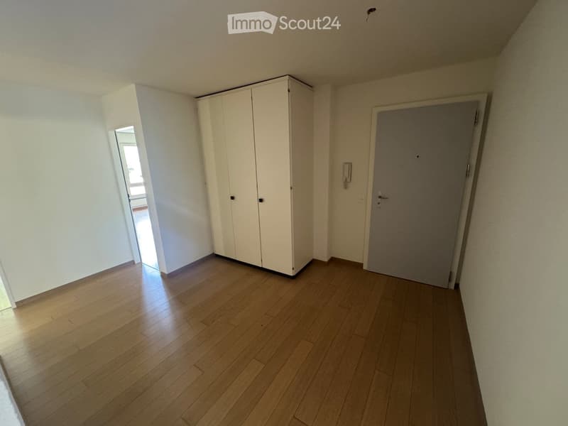 Empty room with wooden flooring, white walls, a closed white wardrobe, and a closed door.