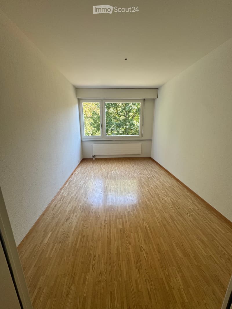 Empty room with wooden flooring, light-colored walls, and a window with a radiator below it.