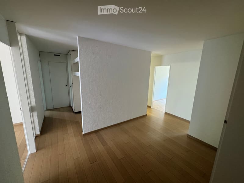 Empty hallway with wooden flooring, white walls, and doors leading to other rooms.