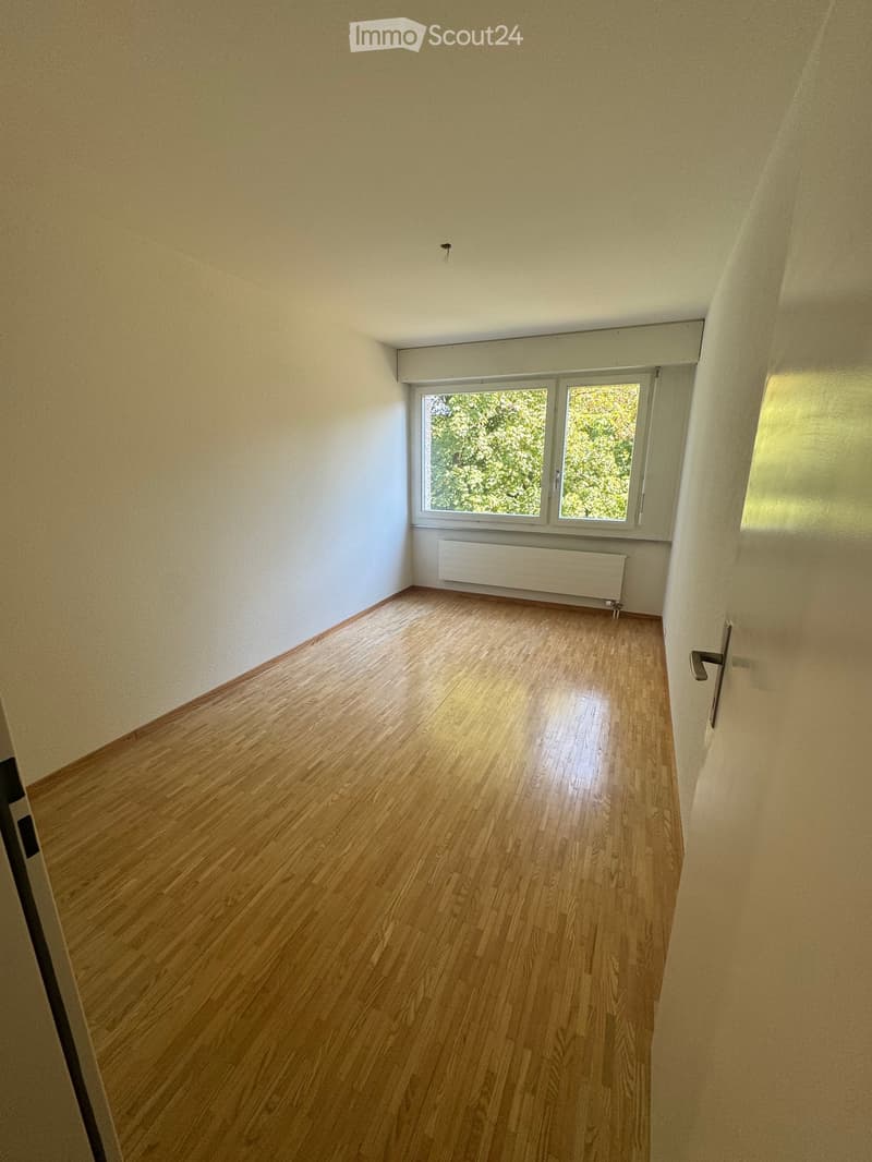 Empty room with wooden flooring, white walls, and a window with a radiator below it.
