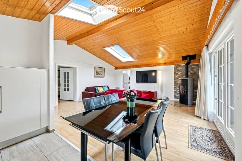 Open-plan living and dining area with wooden ceiling, skylights, red sofa, dining table with chairs, TV, and a fireplace.