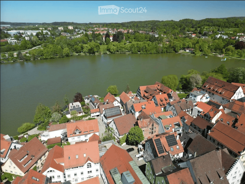 Aerial view of a town with numerous houses, red-tiled roofs, and a lake in the background.