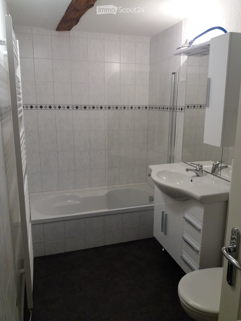Modern bathroom with white tiles, a bathtub, a sink with a faucet, a toilet, and a mirrored cabinet.