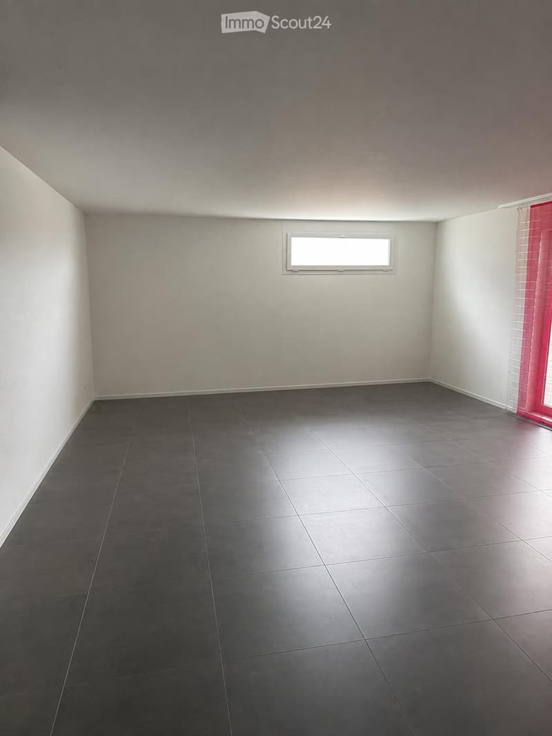 Empty room with grey tiled floor, white walls, and a single window with white frame. No furniture or equipment present.