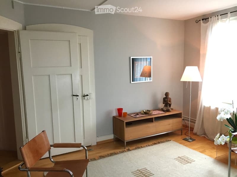 A modern living room with a leather chair, a wooden TV stand, a floor lamp, a picture frame, a small statue, and a white rug on a wooden floor.