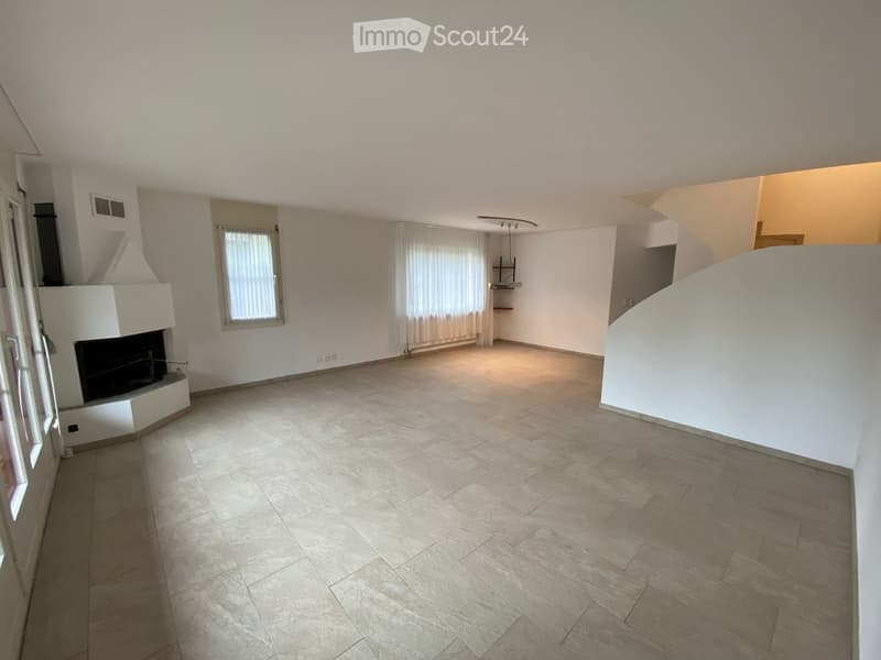 Empty living room with tiled floor, fireplace, large windows with curtains, and a staircase leading to another level.