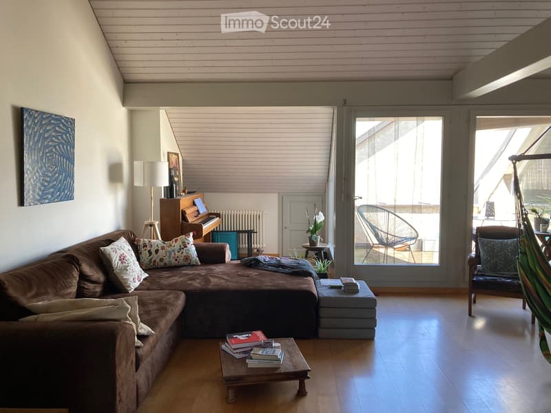 Living room with wooden floor, large window, sofa, coffee table, piano, and a hammock in the corner.