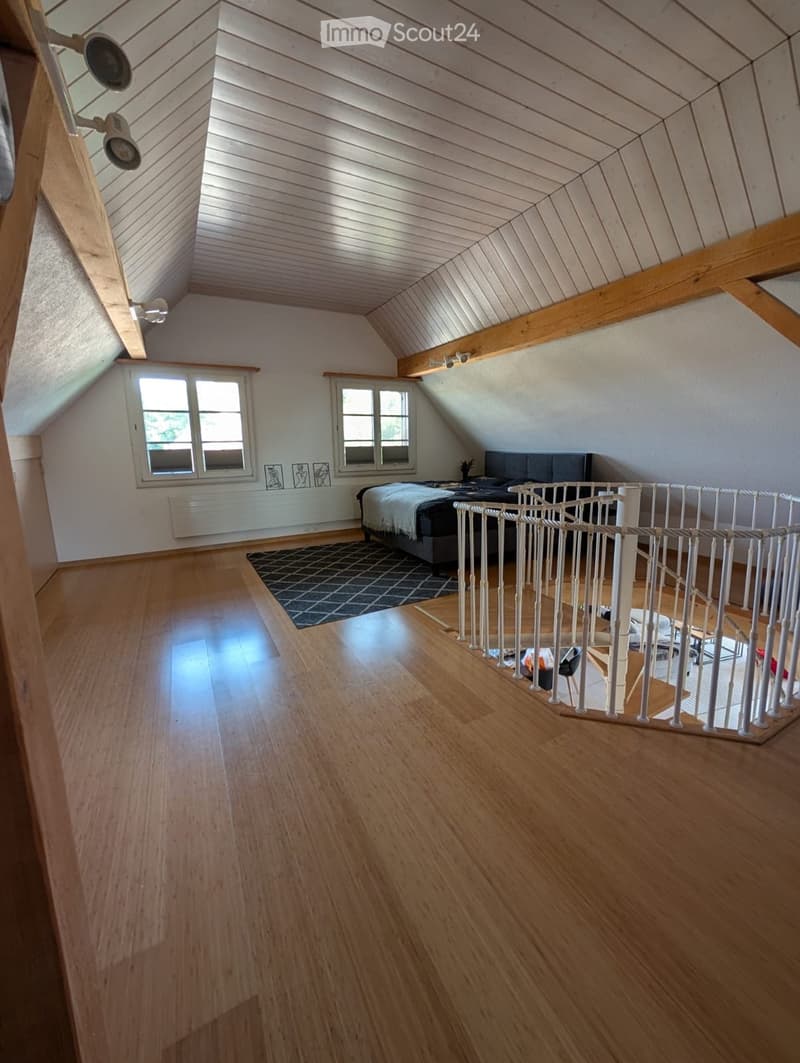 a room with a bed and spiral staircase, white walls, wooden floor, ceiling lights, and windows