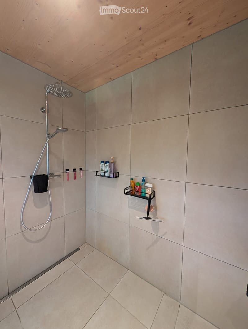 white tiled wall and floor, showerhead and hose, metal shelf with toiletries, wooden ceiling