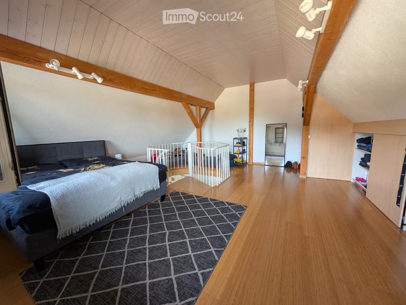 A bedroom with wooden floor, a bed, and a white railing on the stairs