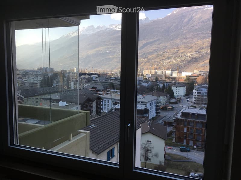 Balcony with expansive view of a cityscape and snow-capped mountains in the background.
