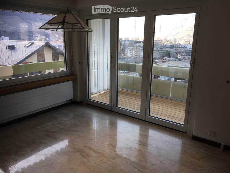 Empty room with large sliding glass doors leading to a balcony, polished stone floor, radiator, and a view of the city and mountains.