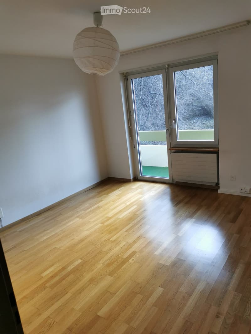 Empty room with light wooden flooring, white walls, a large window with frosted glass, and a hanging paper lantern light fixture.