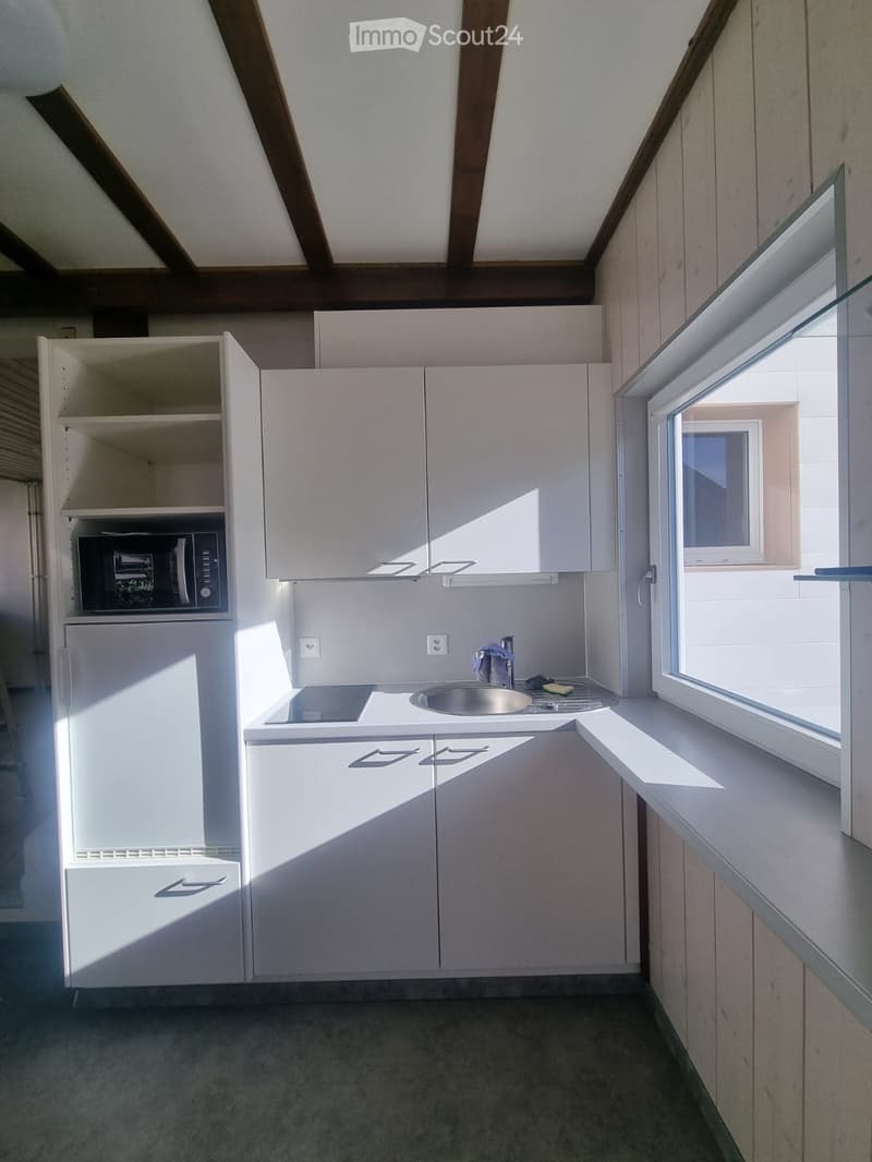 Compact kitchen with white cabinets, microwave, refrigerator, sink, and stove. Natural light from a window on the right.