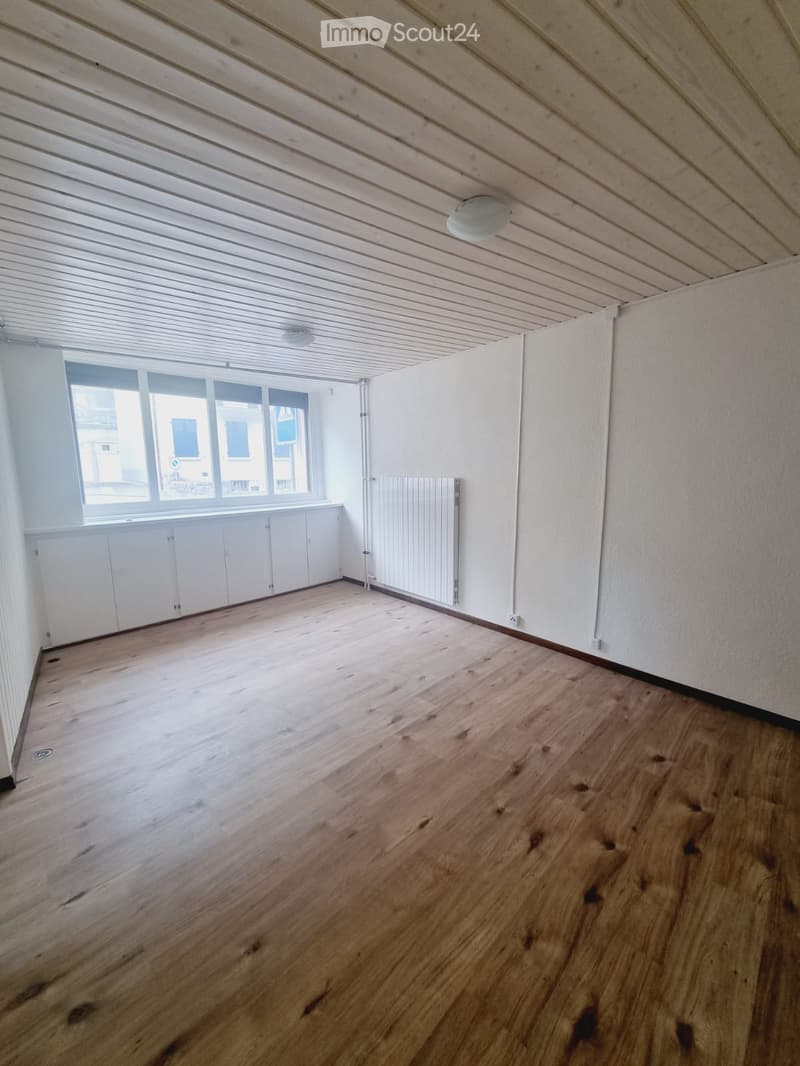 Empty room with wooden flooring, white walls, large window, and built-in cabinets.