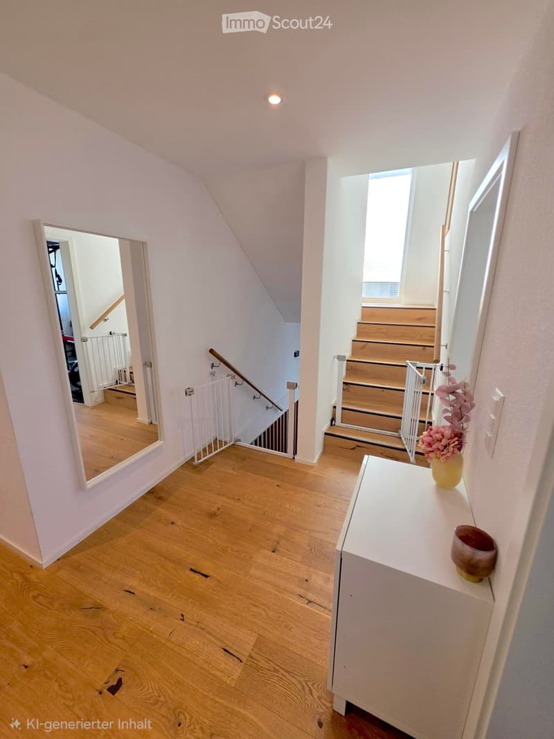 Bright hallway with wooden flooring, white walls, and a small console table holding a vase and a bowl. Stairs lead upwards with a wooden railing and a white baby gate.