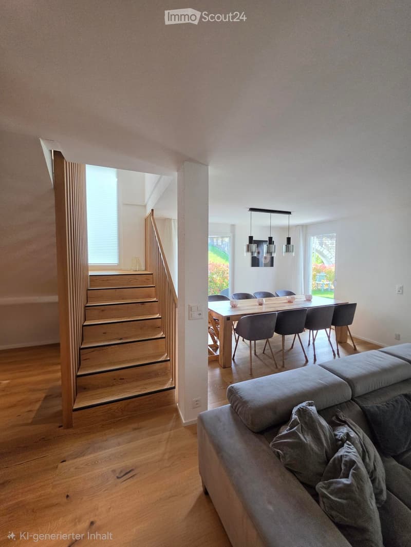 Open-plan living and dining area with wooden flooring, grey sofa, dining table with chairs, pendant lights, and a staircase leading to another level.
