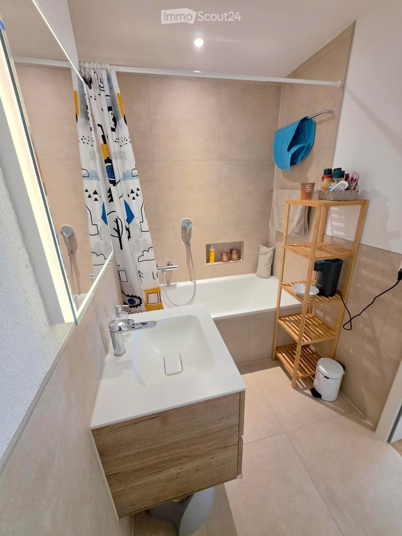 Modern bathroom with a white sink, bathtub, wooden shelf, and various toiletries.