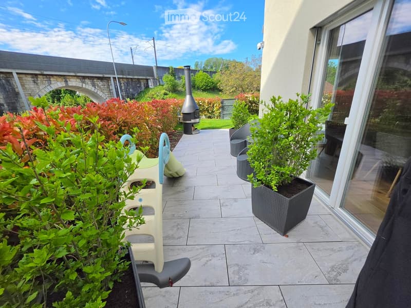 A well-maintained patio area with tiled flooring, potted plants, outdoor seating, and a small fireplace.