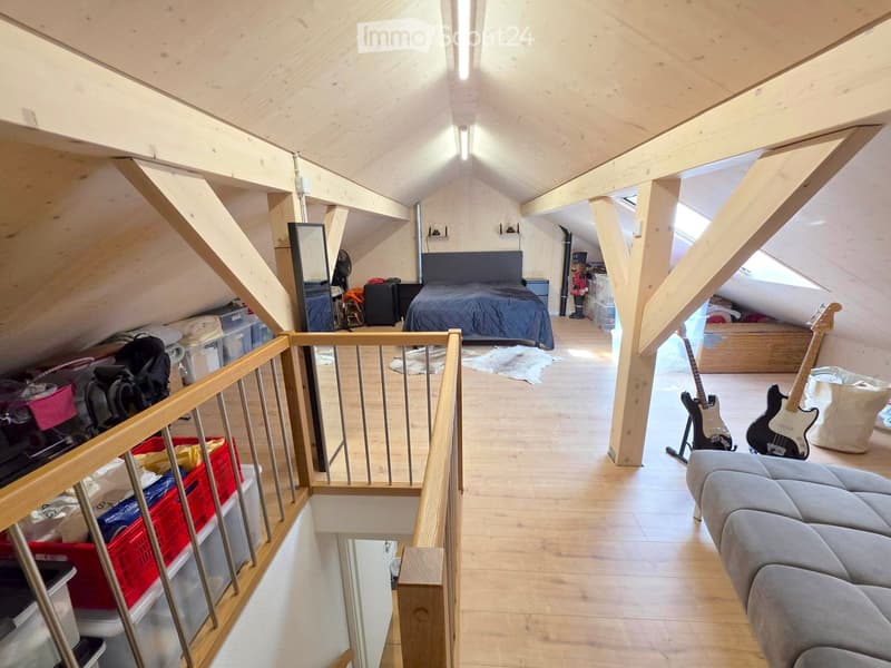 Loft-style bedroom with wooden beams, slanted ceilings, and skylights. Features a sofa, guitars, a bed, and storage bins.