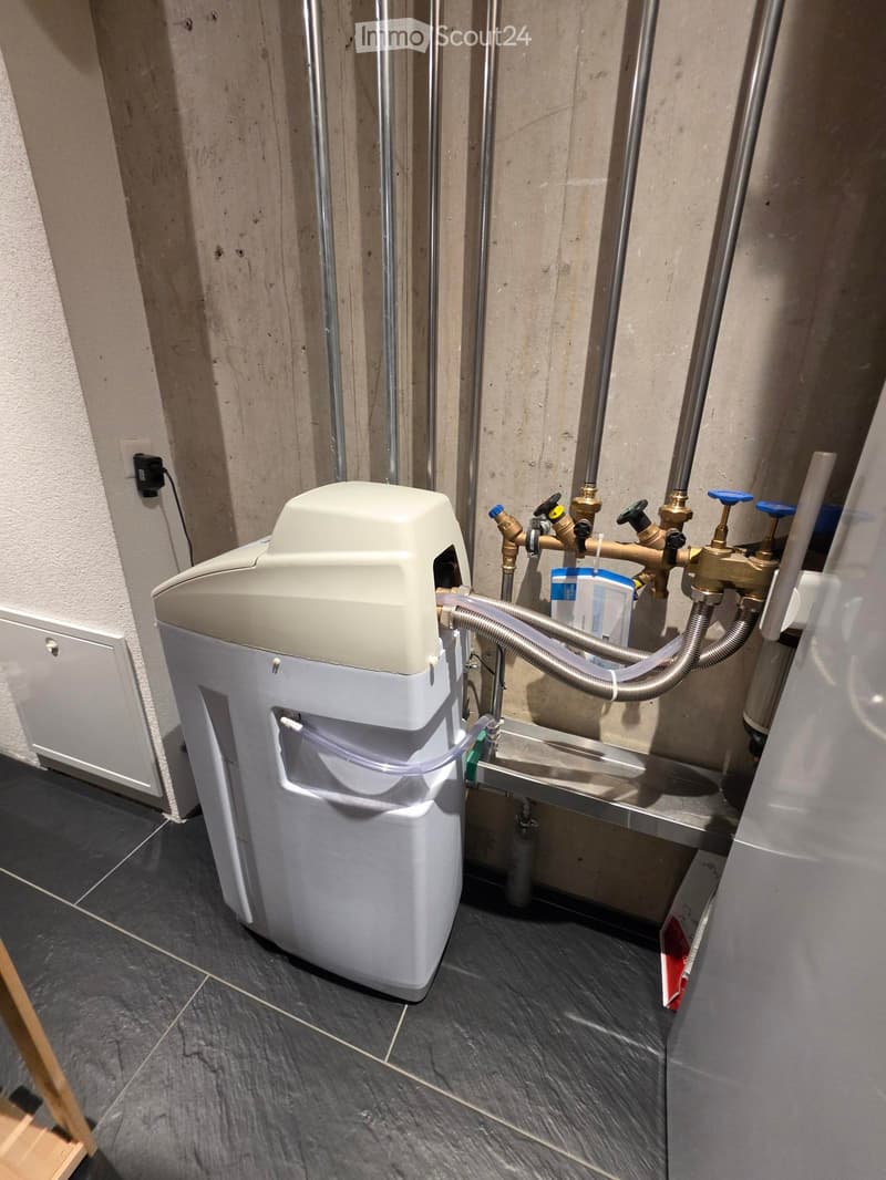 A modern bathroom with a white washing machine, metallic pipes, and a tiled floor.