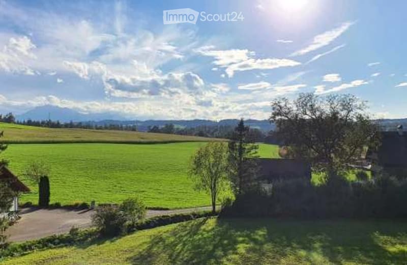 A peaceful countryside scene with green fields, scattered trees, and a small wooden structure under a partly cloudy sky.