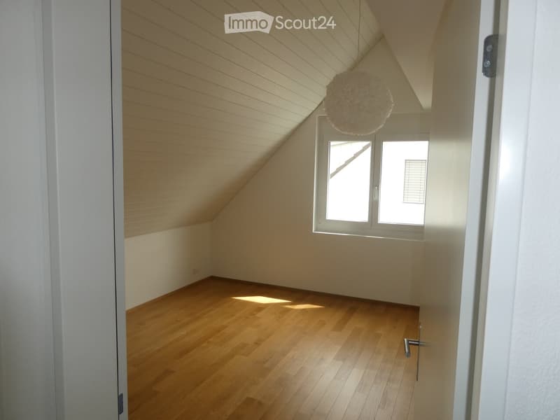 Empty attic room with wooden floors, white walls, and a skylight window. The room features exposed wooden beams on the ceiling and a hanging decorative ball light fixture.