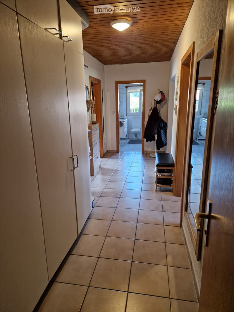 A clean, tiled hallway with wooden doors and a coat rack. Visible rooms include a bathroom and a small storage area.