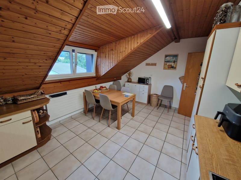 Cozy kitchen with wooden ceiling, tiled floor, and large window. Includes a dining table with chairs, microwave, and various kitchen cabinets.
